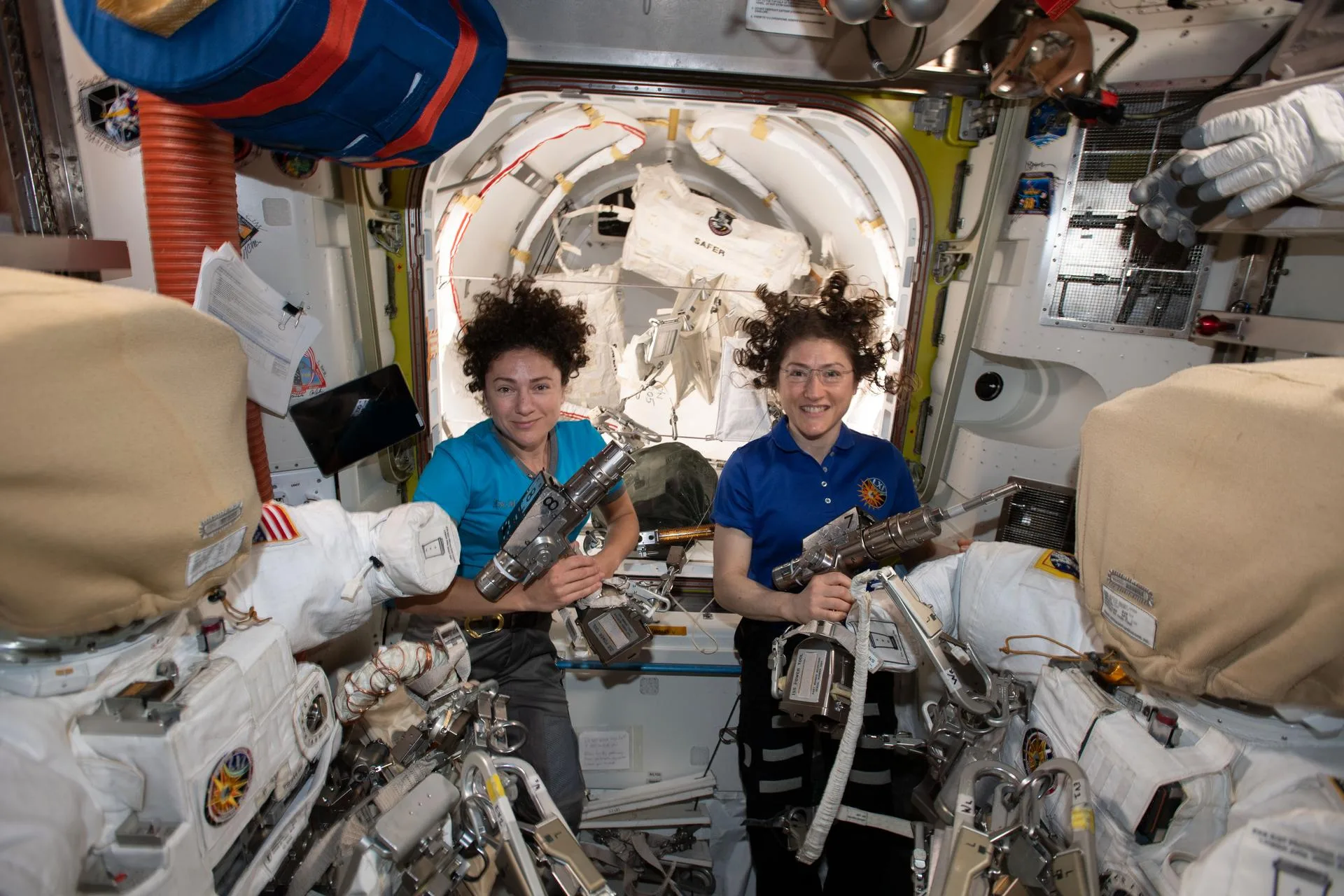 NASA astronauts Jessica Meir (left) and Christina Koch are inside the Quest airlock preparing the U.S. spacesuits and tools they will use on their first spacewalk together. The Expedition 61 flight engineers are holding the pistol grip tools they will use to swap out a failed power controller, also known as a battery charge-discharge unit, that regulates the charge to batteries that collect and distribute power to the International Space Station.